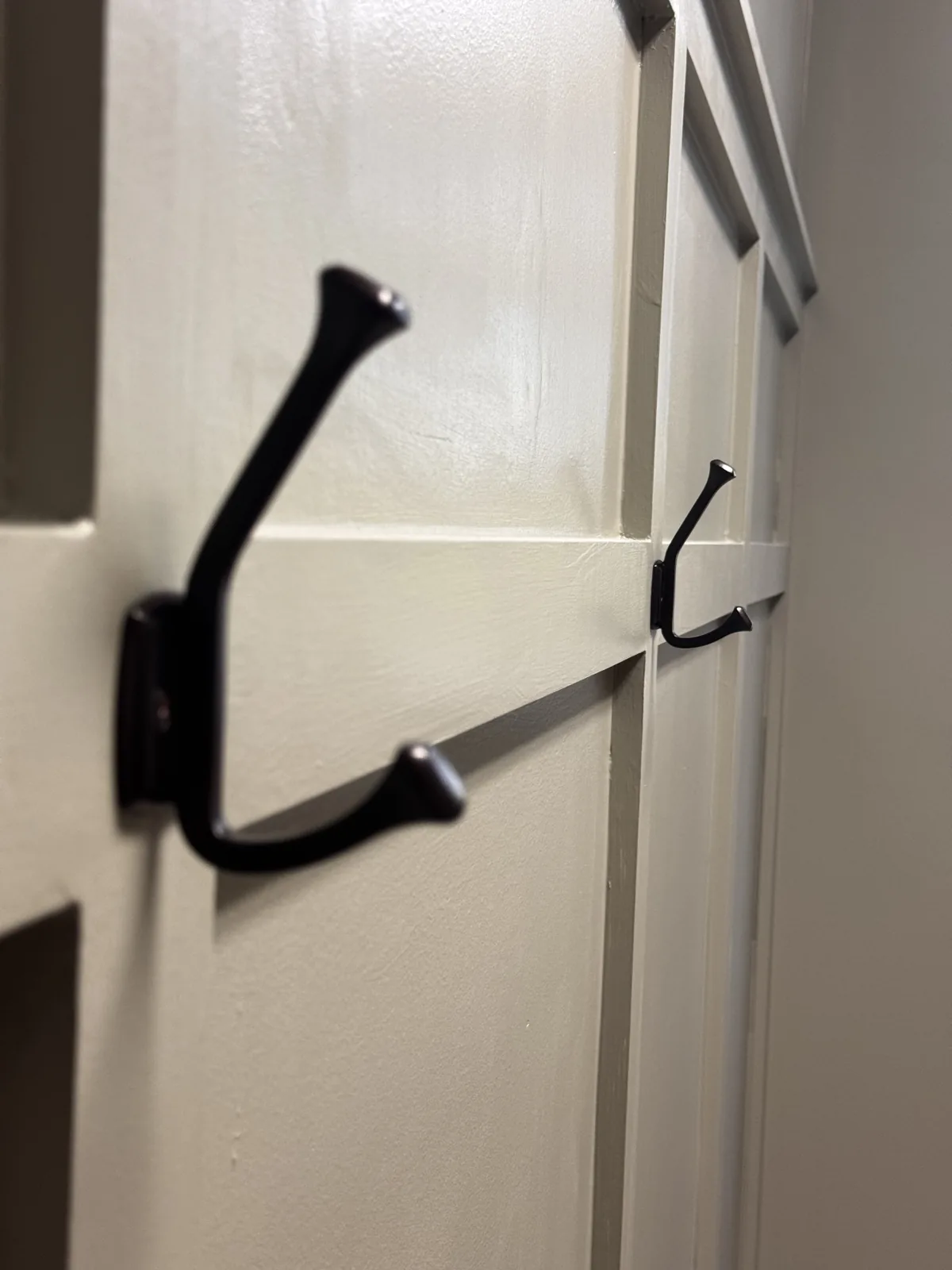 Black coat hooks installed on painted panel molding